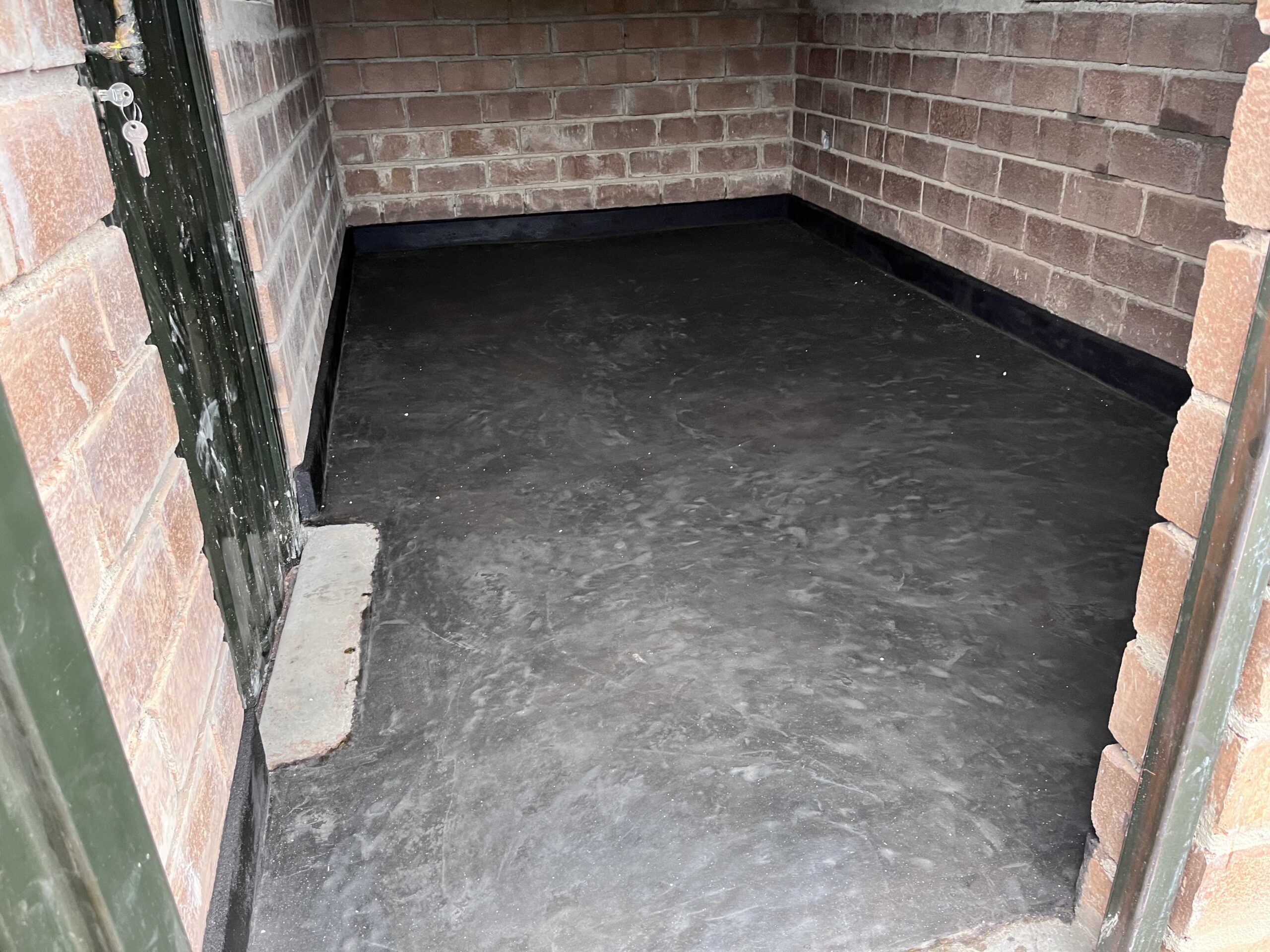 A large structure with numerous solar panels on the roof is visible, suggesting an eco-friendly or energy-efficient building. The building has a modern design with multiple windows and a blue color scheme. A blue, sloped walkway or canopy is present, leading from one section to another. The surrounding area includes green grass and some trees, with a bright, partially cloudy sky overhead.