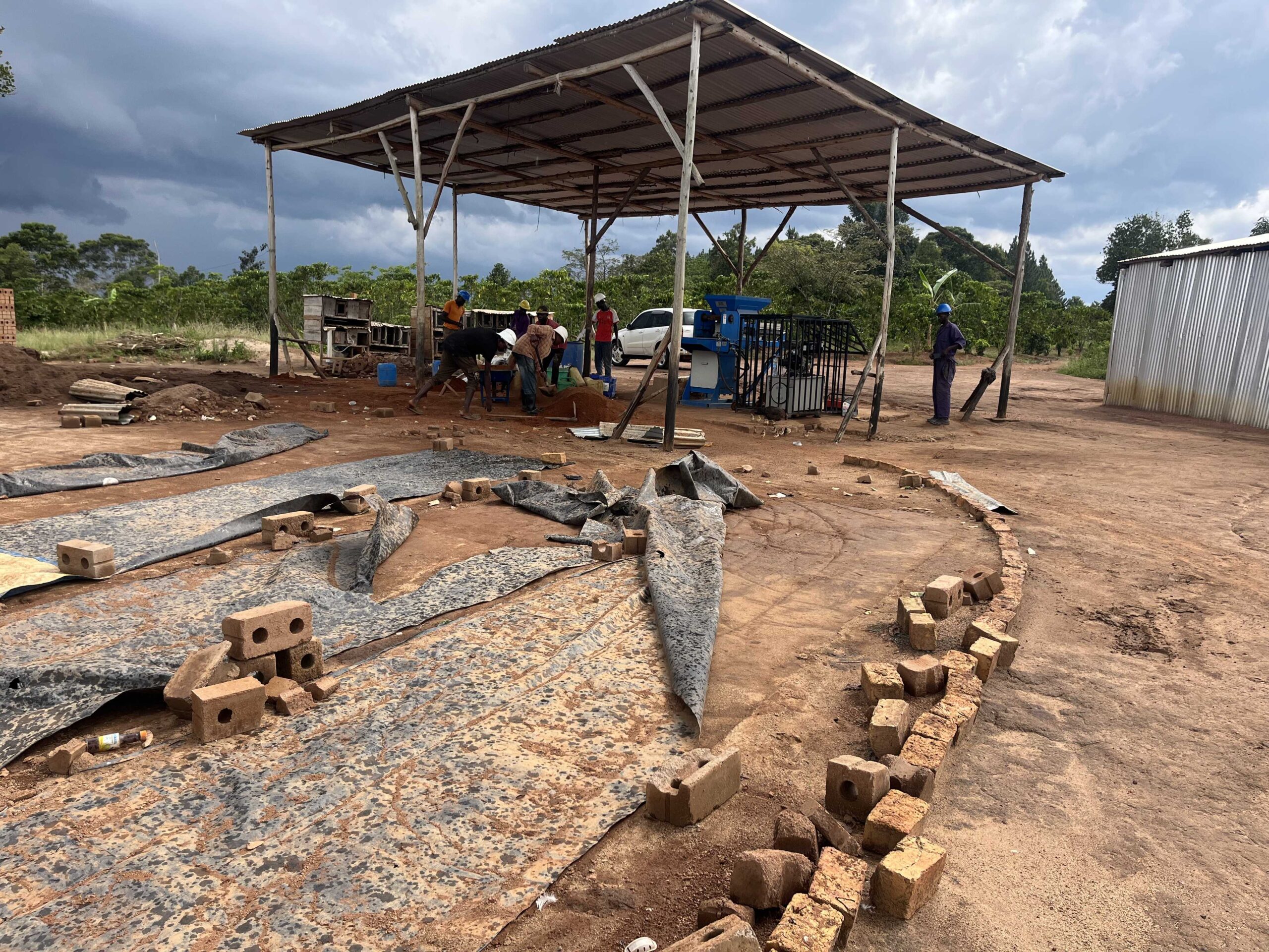 An architectural structure composed of stacked modular concrete units, creating a geometric and futuristic appearance. The building features numerous windows and terraces, surrounded by some sparse landscaping and trees.