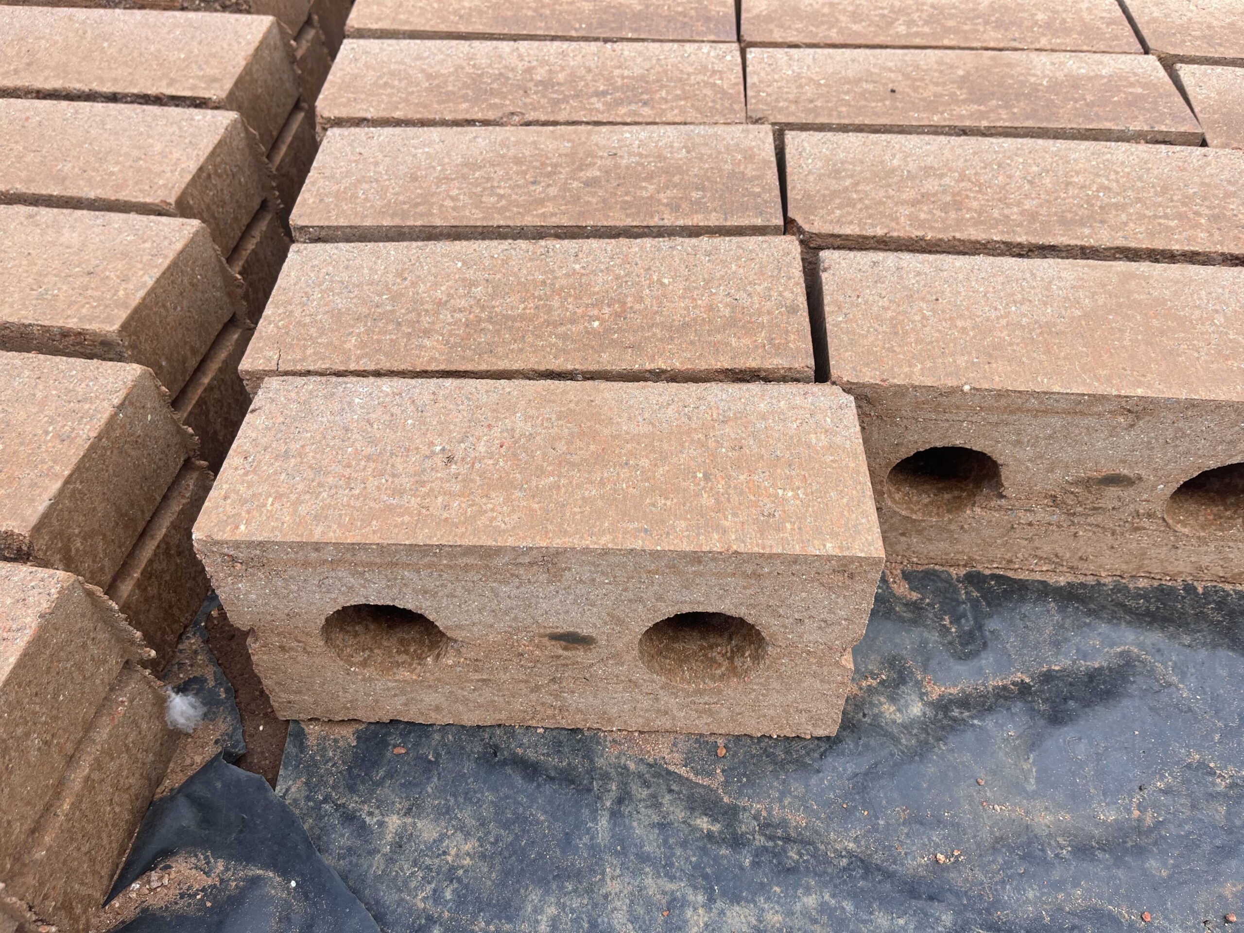 A small wooden house with a modern design is situated on a sloping grassy hillside. The house has solar panels installed on the roof. The landscape includes rolling hills and mountains in the distance, covered with dense forests. The sky is cloudy and overcast, suggesting an impending storm or recent rainfall.